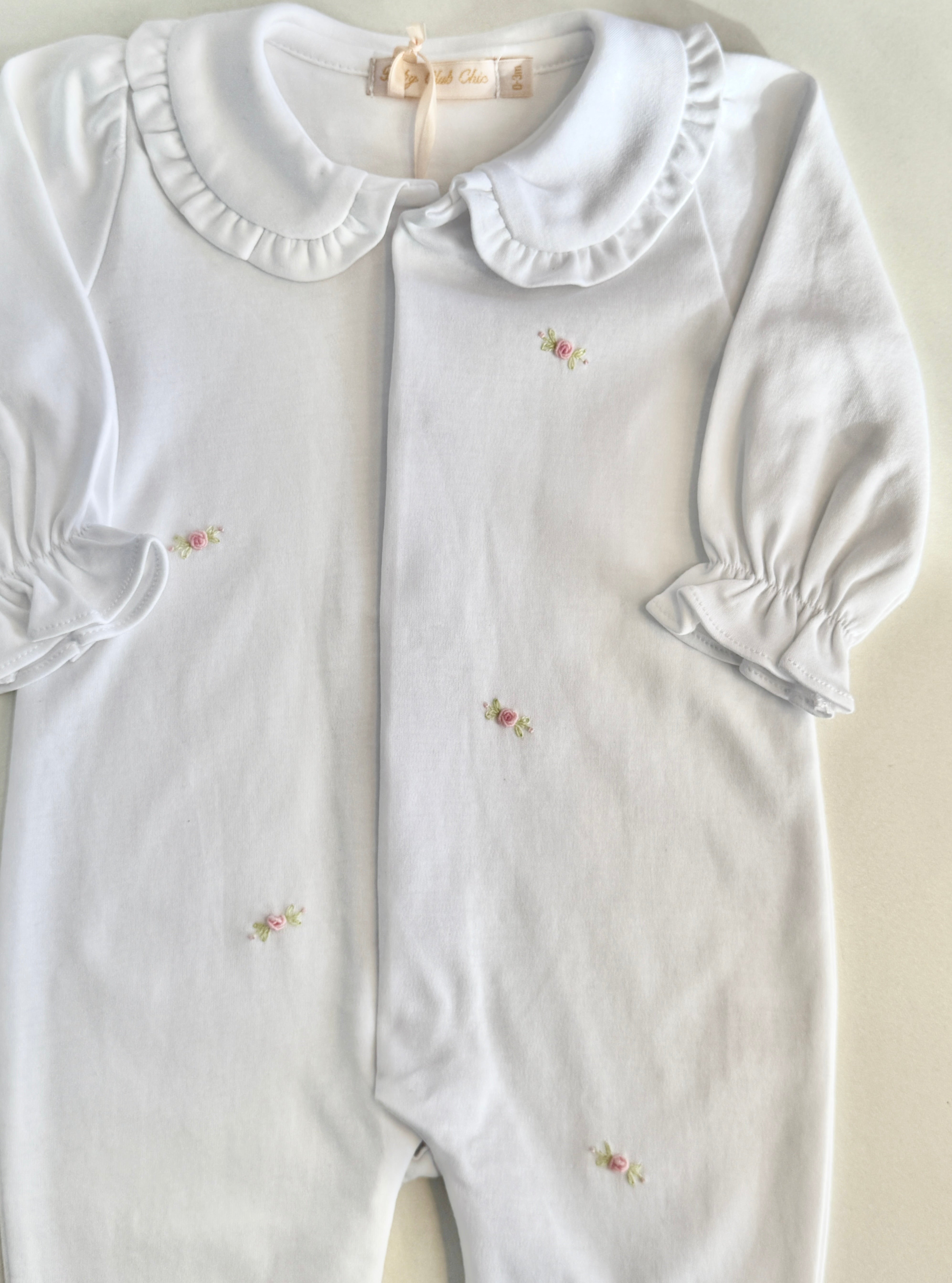 White baby romper with ruffled collar and embroidered details on a light background